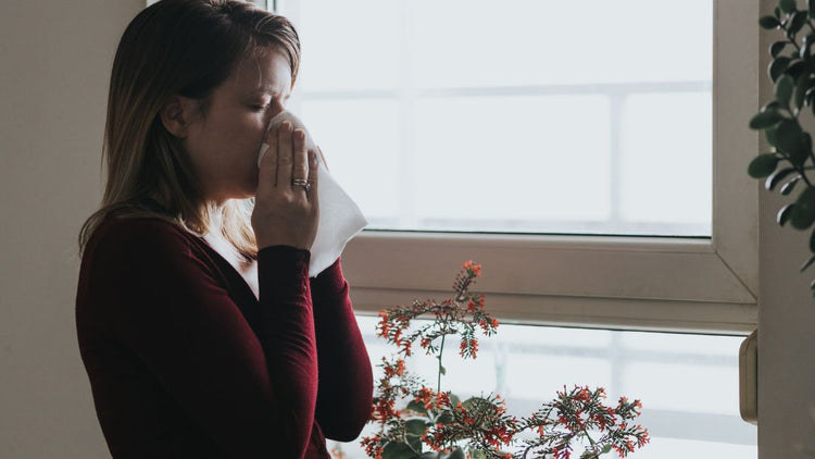Woman with allergy symptoms beside a rain-covered window during autumn
