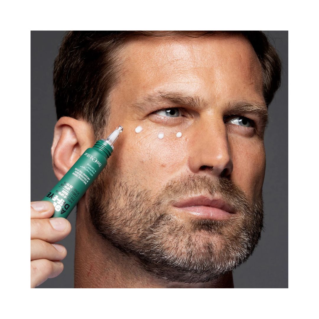 Bearded man applying Shakeup Age Def-Eye Instant Lifting Eye Cream to his eye on a grey background