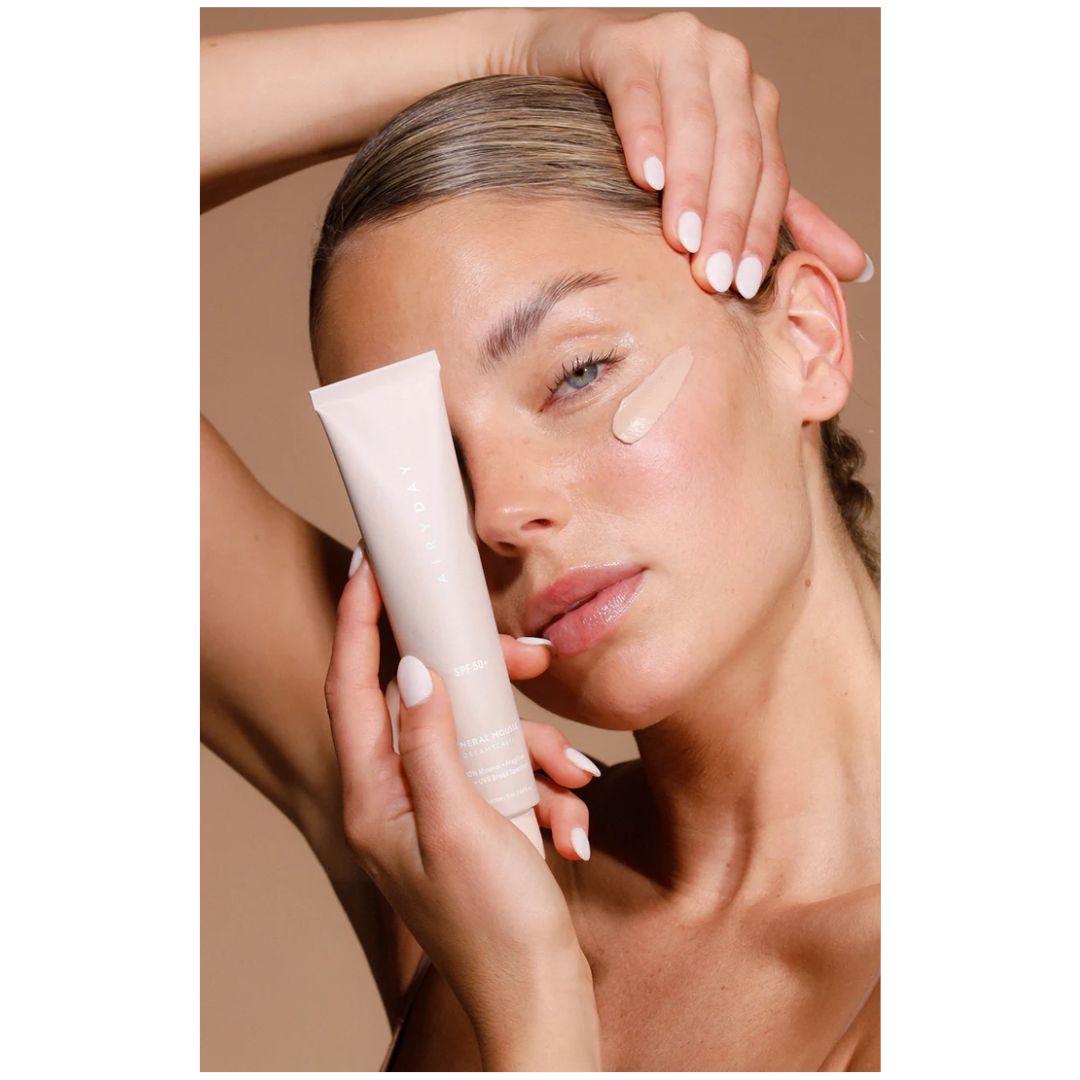 Airyday Mineral Mousse SPF50+ Dreamscreen being held by a woman with a smear of the product on her cheek