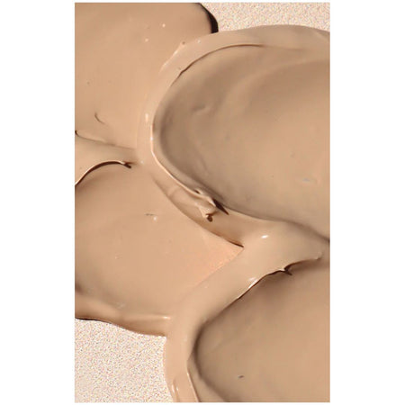 A close-up of thick, smooth beige cream or liquid makeup swirled on a light textured surface.