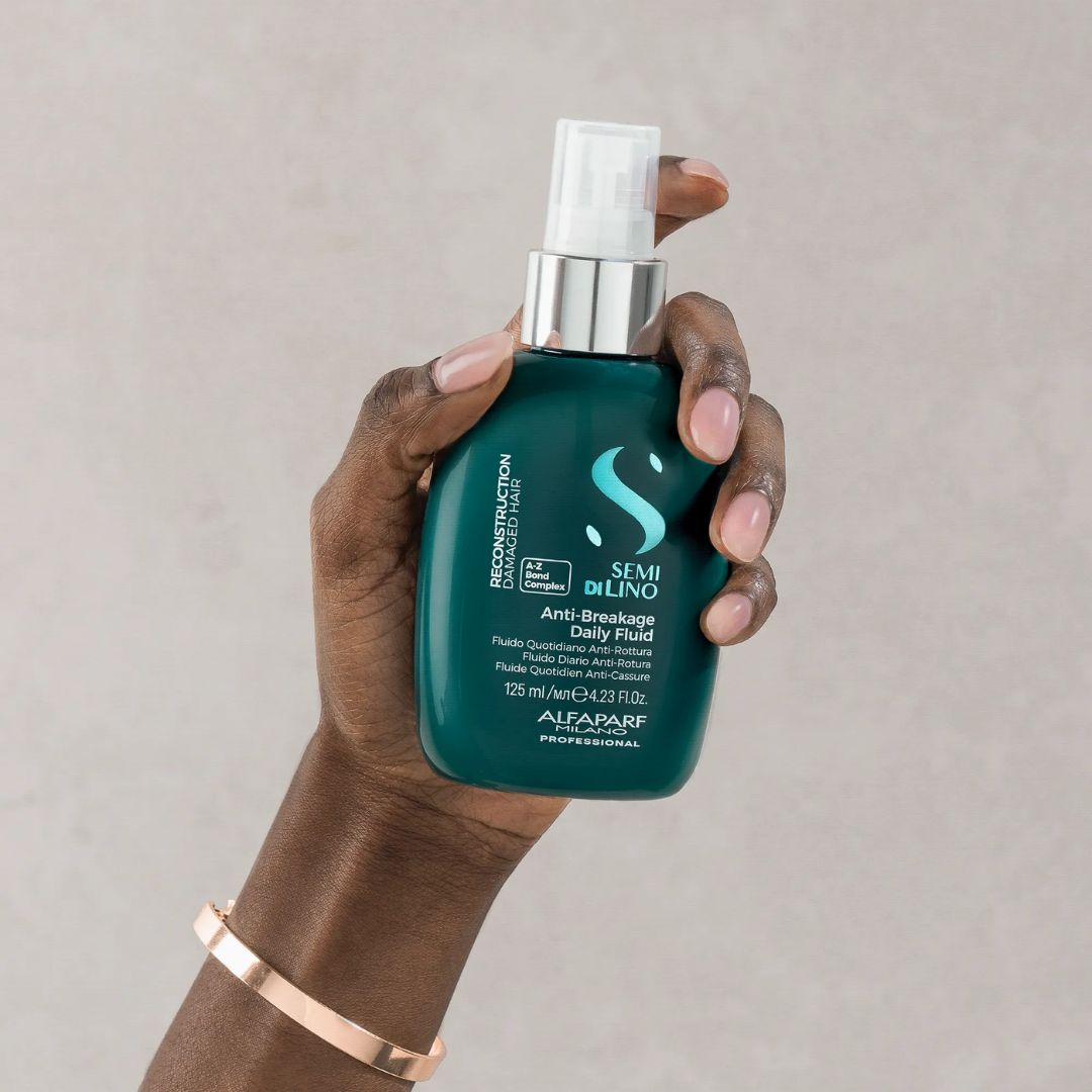 Hand holding a green hair care product bottle against a neutral background
