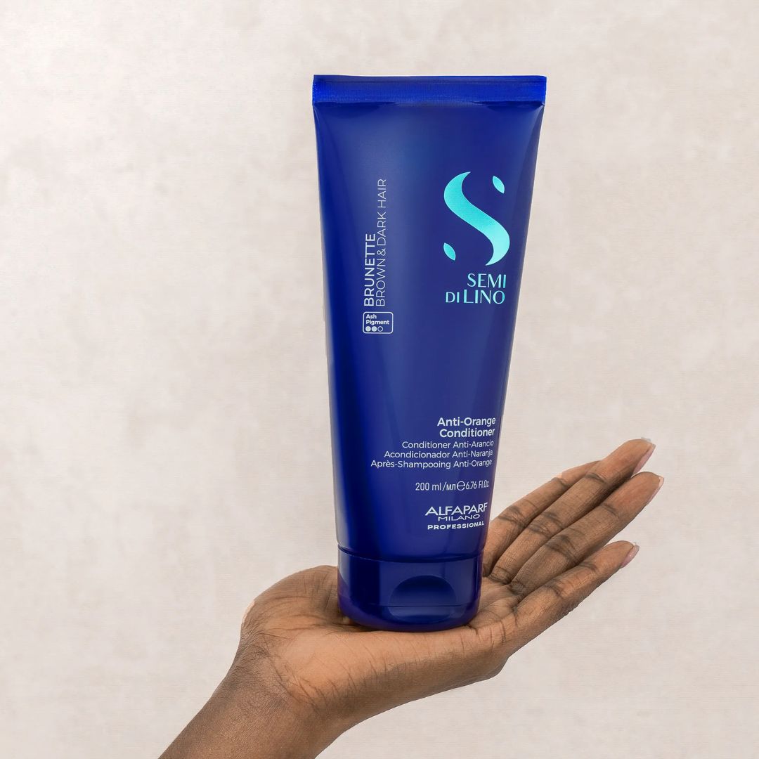 Blue conditioner bottle held in a hand against a beige background