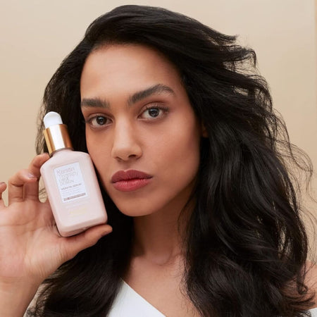 Woman holding a pink skincare bottle against a beige background