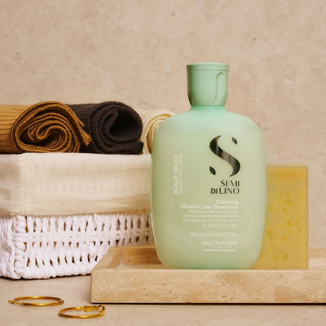 Green bottle of Semi di lino hair care product on a wooden surface with towels and rings in the background.