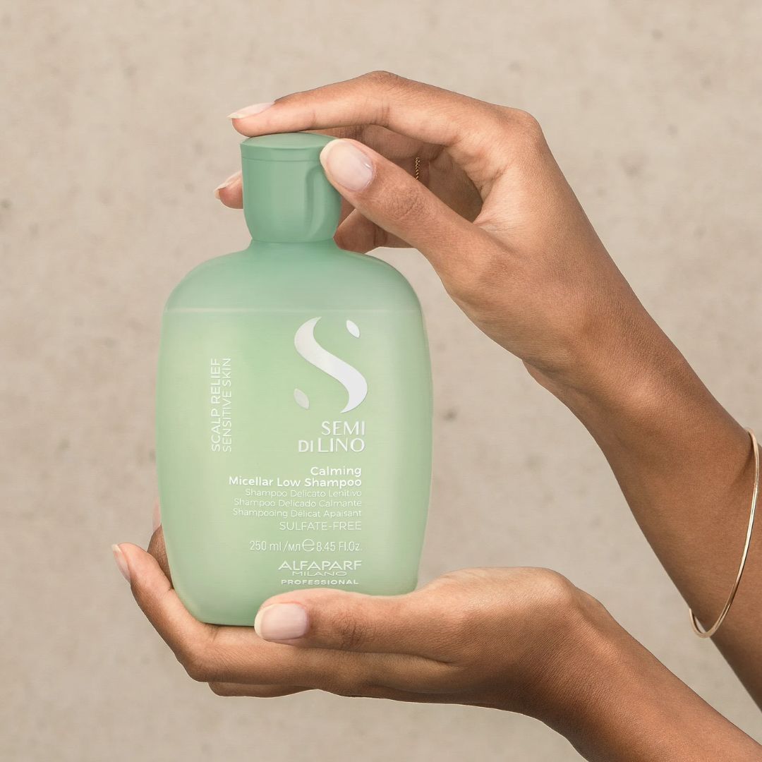Hand holding a green bottle of Alfaparf Semi Di Lino hair product against a beige background