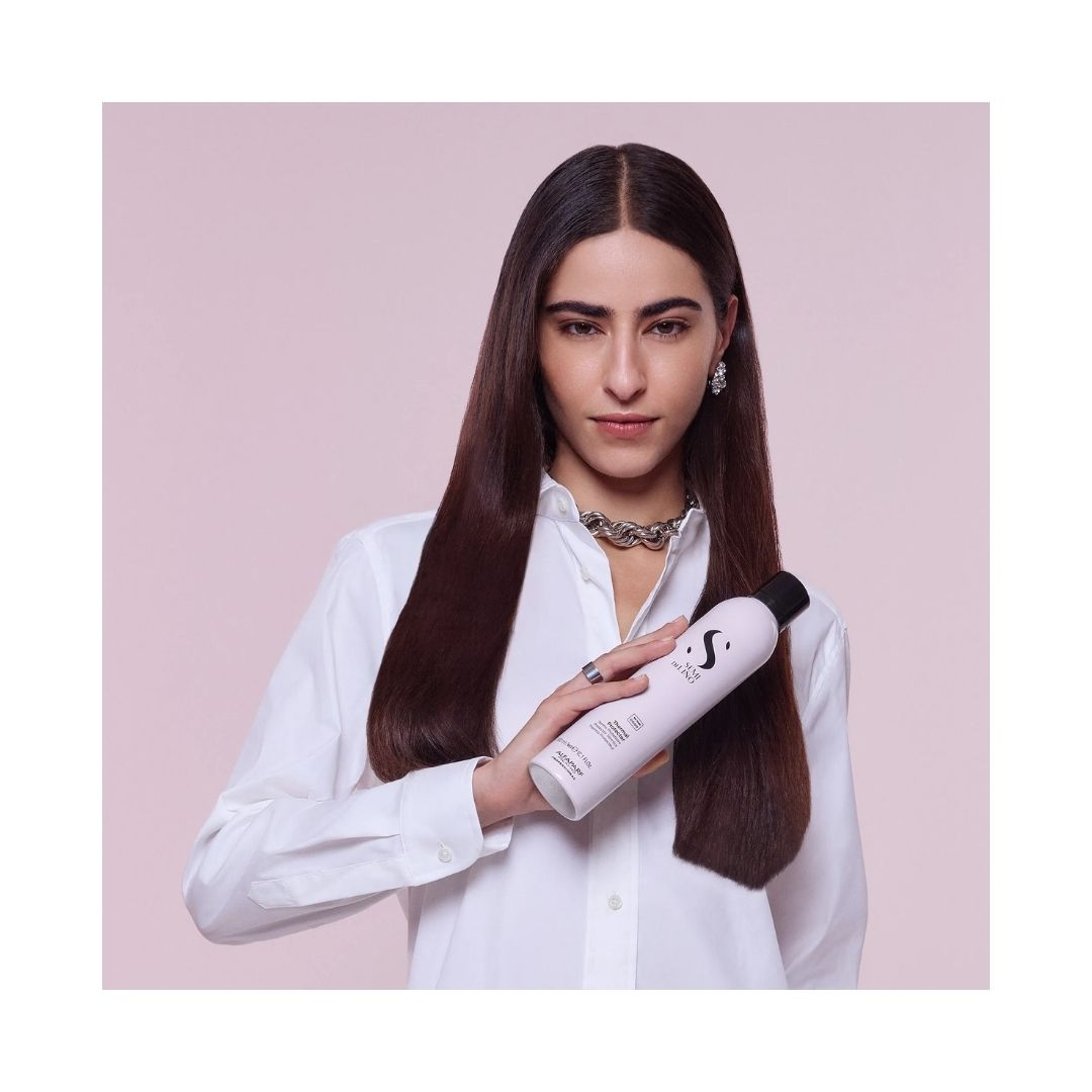 Alfaparf Milano Semi di Lino Thermal Protector 300ml being held by a black haired woman in a white shirt on a grey background