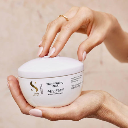 Hand holding a jar of Alfaparf Illuminating Mask against a beige background