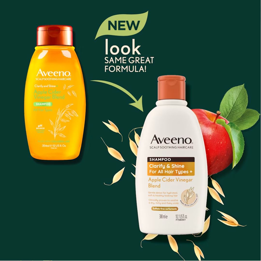 Aveeno Clarify & Shine Scalp Soothing Haircare set featuring a yellow-orange shampoo bottle and a white conditioner bottle with a copper cap, shown on a dark green background with an apple and oat graphics and a 'NEW look SAME GREAT FORMULA!' banner.