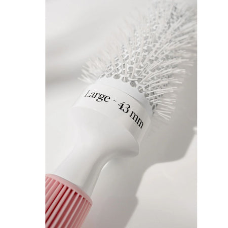 A close-up of a round hairbrush with white bristles, a white handle, and a pink ribbed grip. A white label on the handle reads 'Large - 43 mm'.