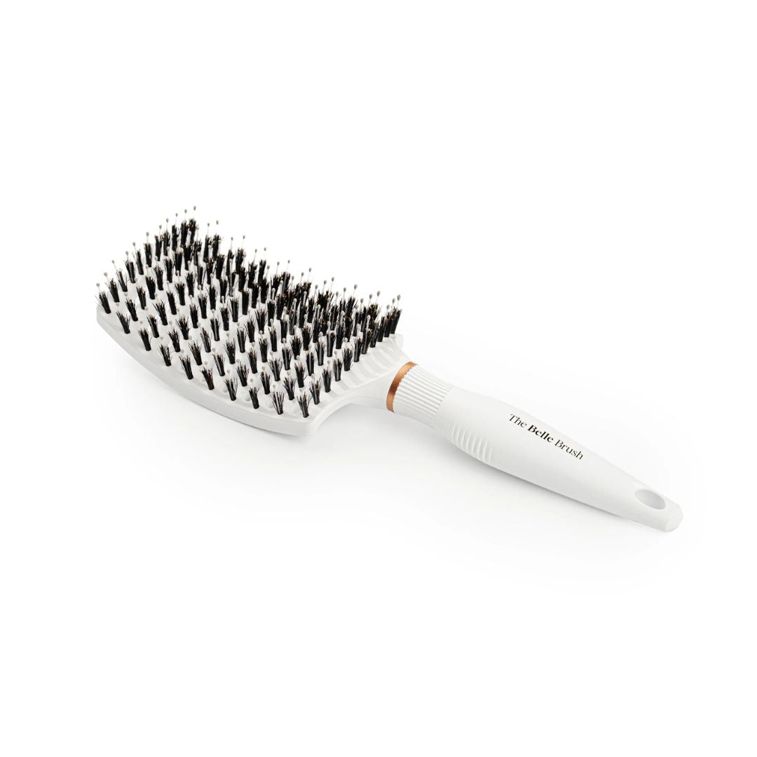 A white paddle hairbrush with black bristles and a small copper accent ring, shown on a clean white background. The handle is printed with the brand name 'The Belle Brush'.