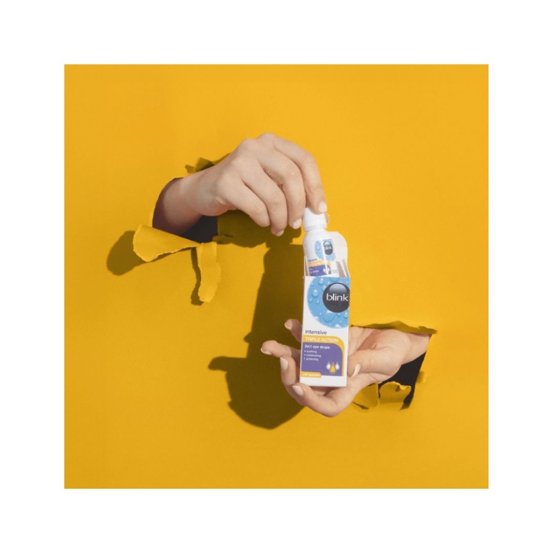 Blink Intensive Triple Action Eye Drops being held in a persons hands on a yellow background