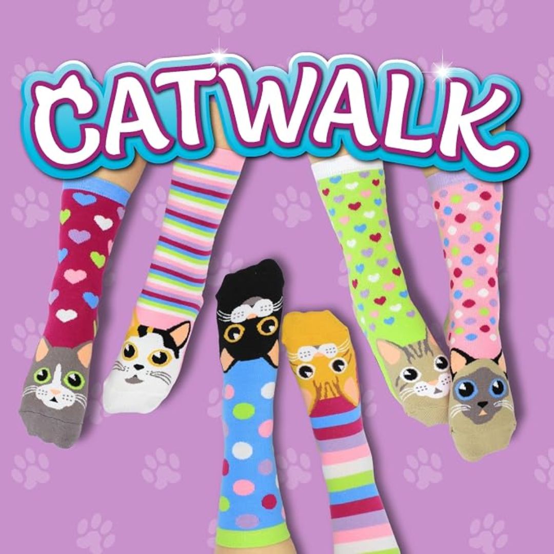 Six novelty socks with cat-themed designs are shown against a lavender background with paw prints and the word 'CATWALK' in large letters. The socks feature different cat faces, stripes, hearts, and polka dots.