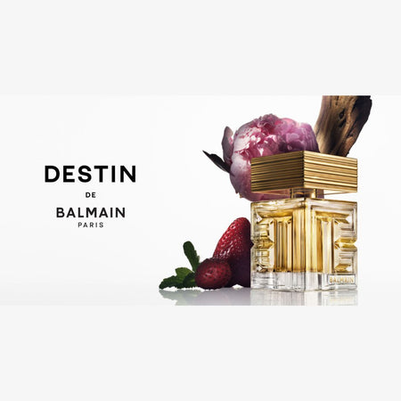 Perfume bottle with flowers and fruits on a white background, featuring the brand 'Destin de Balmain'.