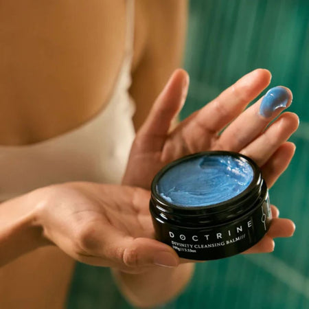 Person holding a jar of blue balm with 'Doctrine' branding.