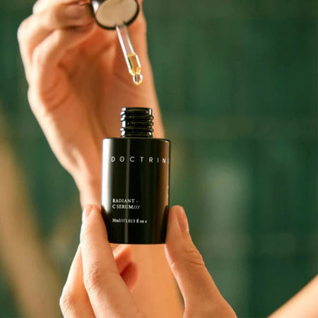 Person holding a black Doctrine serum bottle with a dropper.