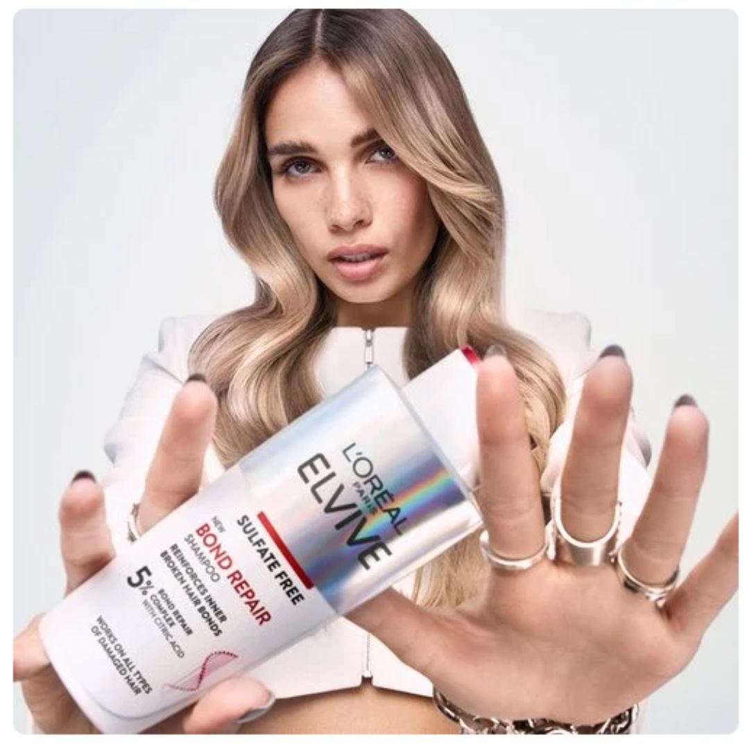 A woman holding a bottle of L'Oréal Paris Elvine Sulphate Free Bond Repair hair color in a studio setting.