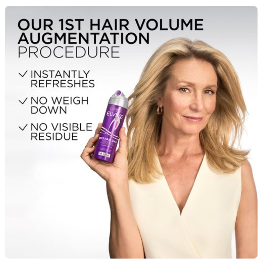 A woman with blonde hair holds up a purple can of Elvive Hair Volume Augmentation spray against a light gray background with promotional text.
