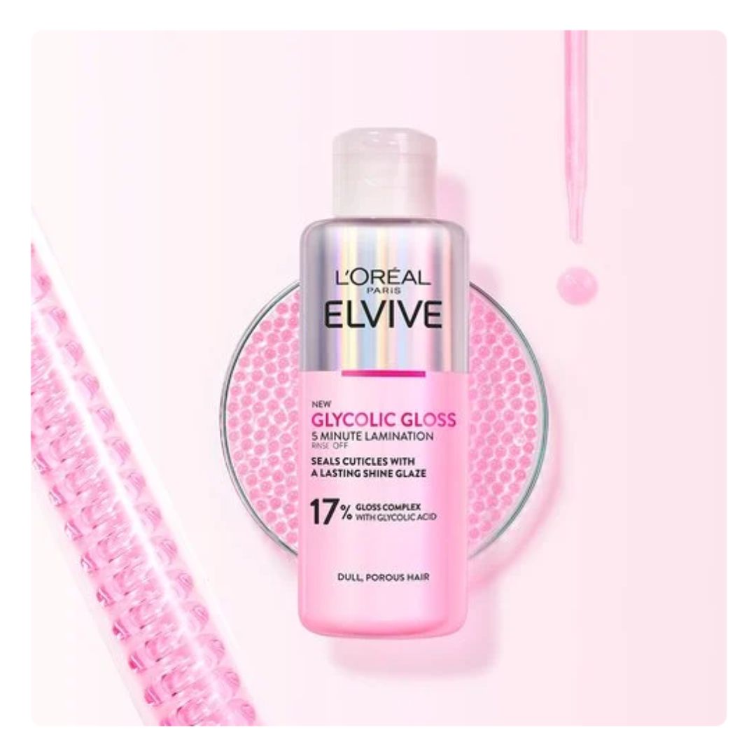 L'Or’ Paris Elvive Glycolic Gloss treatment bottle in pink, displayed on a matching pink circular tray with a pink dropper pipette and textured pink bar in a clean studio setting.