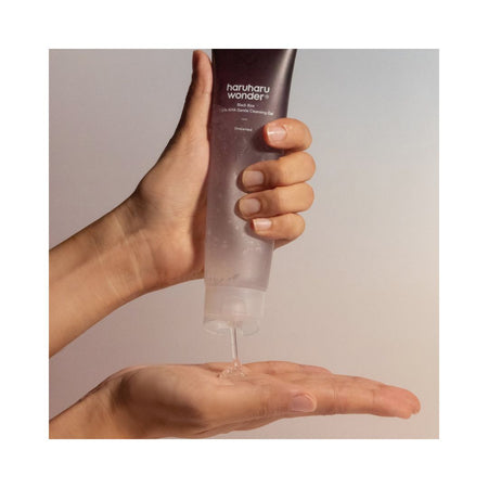 A hand holding a dark brown squeeze tube labeled 'harshu wonder' above another hand, with a clear gel being squeezed onto the palm against a soft beige background.