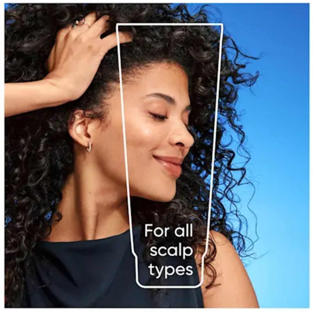 A woman with long, curly dark hair is shown in profile against a bright blue sky, with a white outline and the text 'For all scalp types' overlaid on the image.
