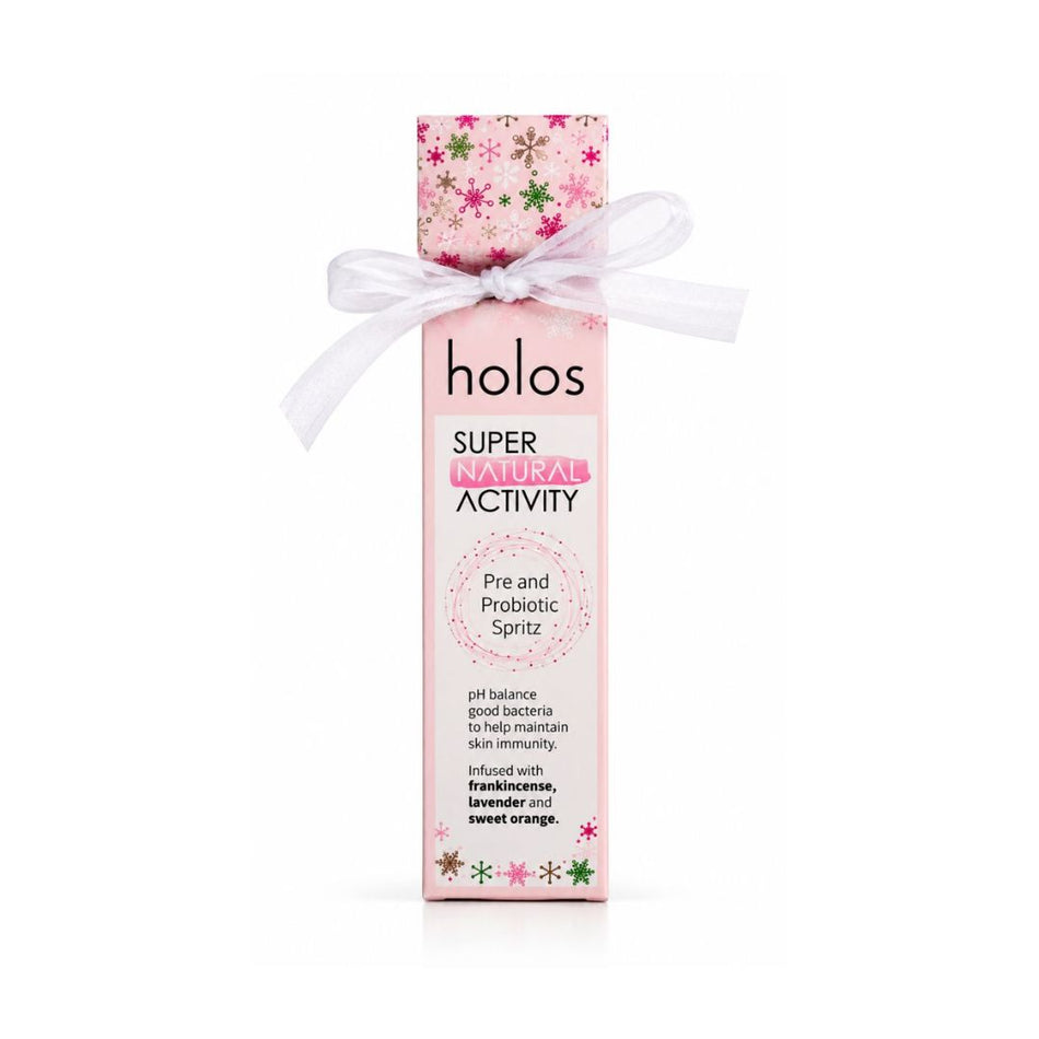 A pink bottle of holos Super Immune Activity Pre and Probiotic Spritz, decorated with a white ribbon bow and a floral cap, on a white background.