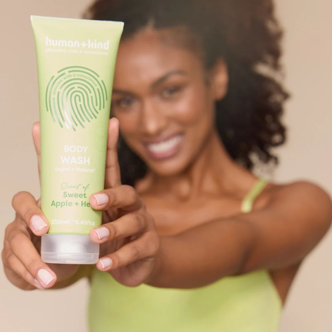 Human+Kind Sweet Apple + Herb Body Wash 250ml being held to the camera by a woman in a green top