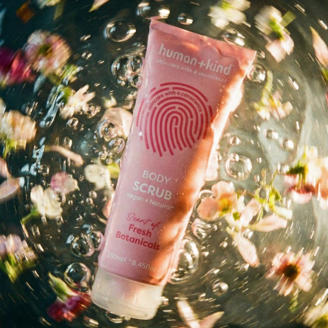 Human+Kind Fresh Botanicals Body Scrub 250ml under water and surroundede by flowers and yellow light