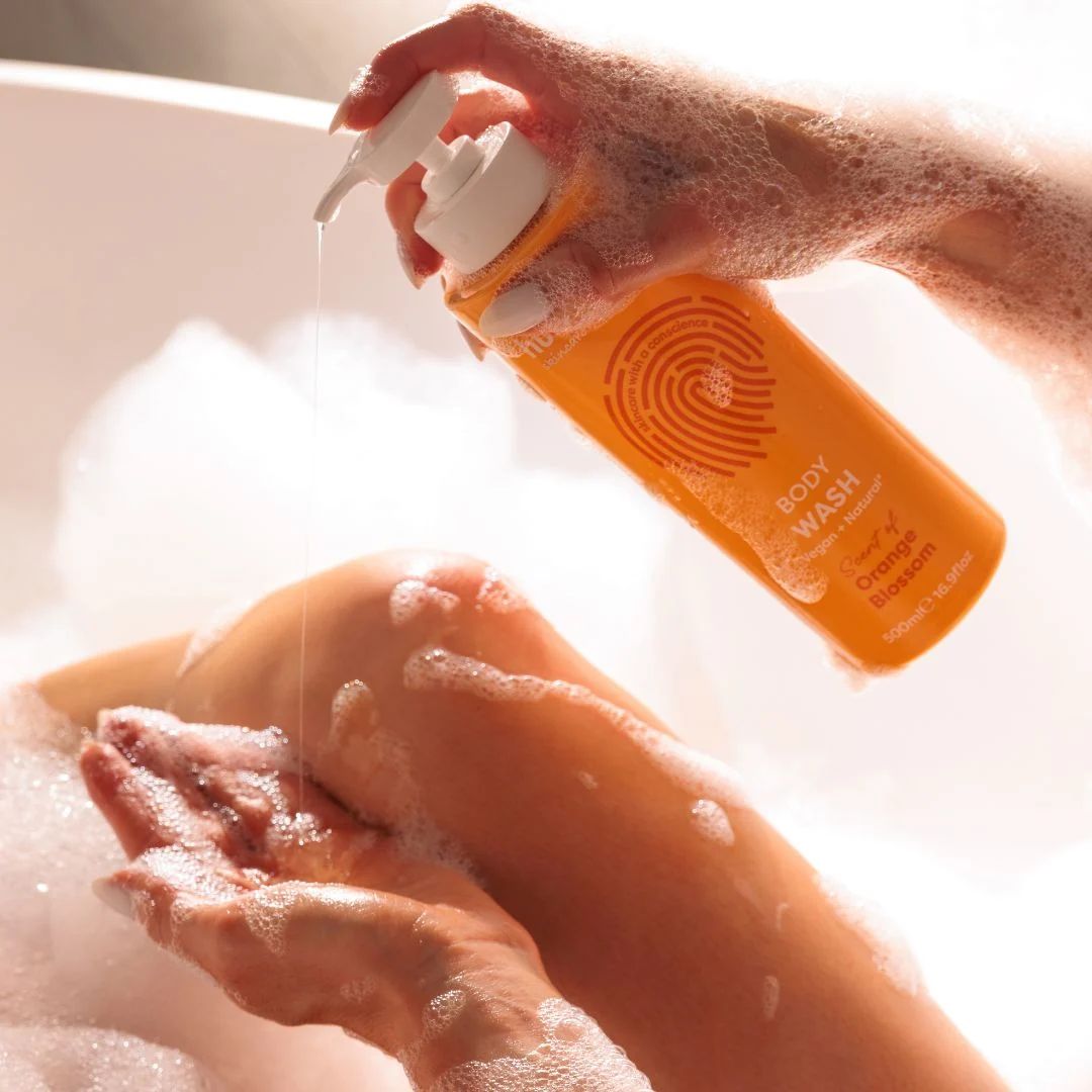 Human+Kind Orange Blossom Body Wash  being poured into a woman's hand in a bubble filled path