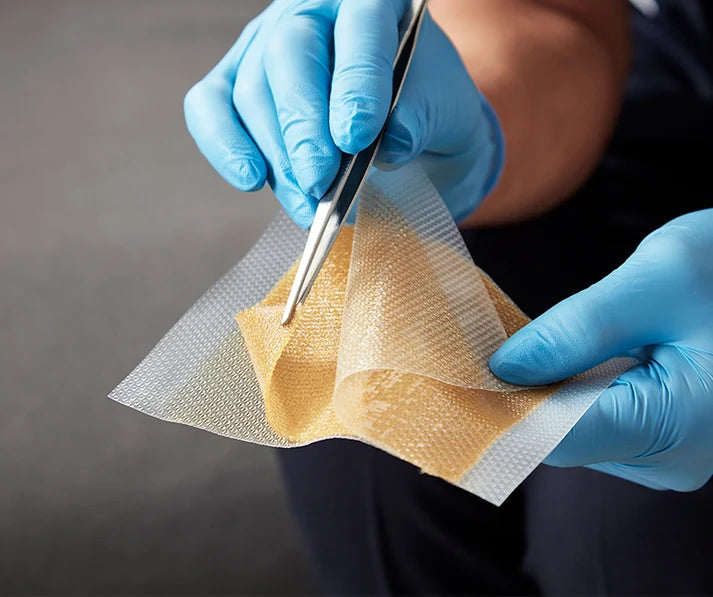 Close-up of hands wearing blue nitrile gloves holding a translucent, textured mesh sheet with tweezers over a dark gray background.