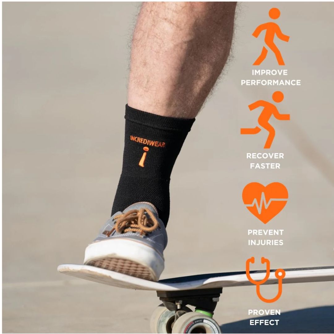 A person's leg and foot wearing a black Incrediwear ankle support while riding a skateboard on a sandy surface. The sock has orange text and a logo.