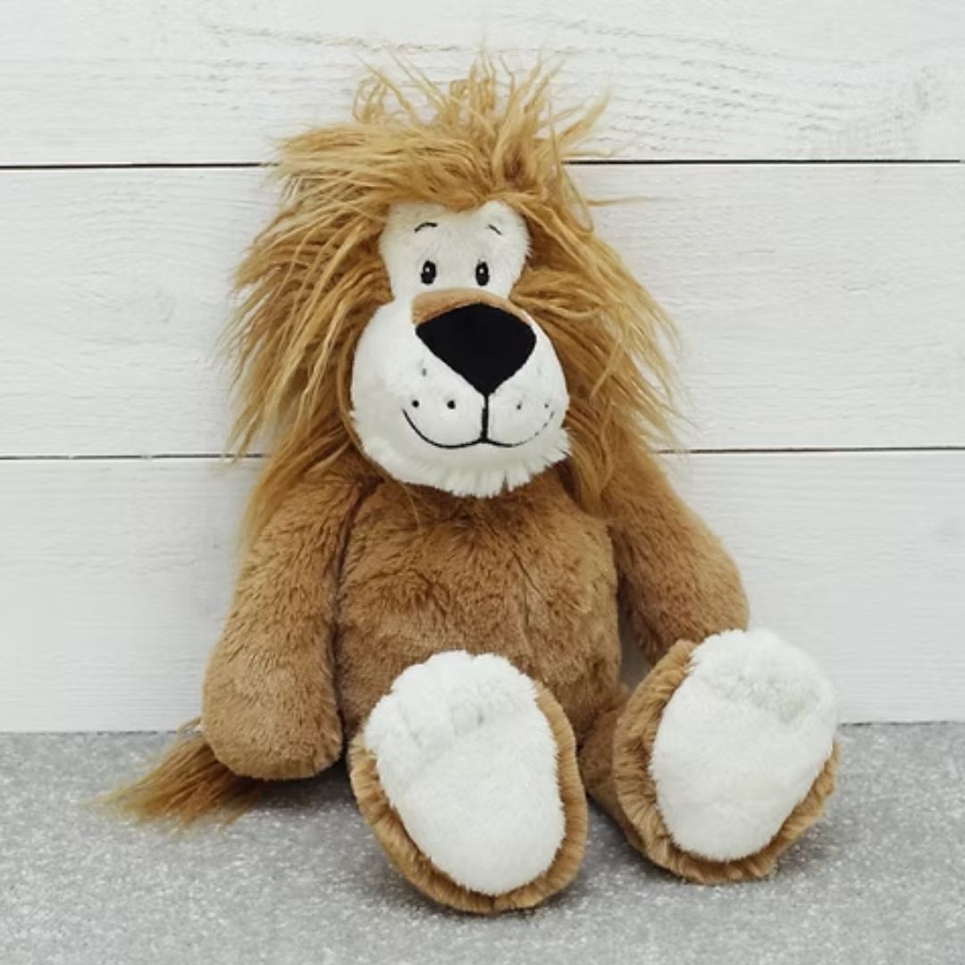 A plush lion toy with a golden-brown shaggy mane, white face and paws, and a black nose, sitting against a white wood plank background.