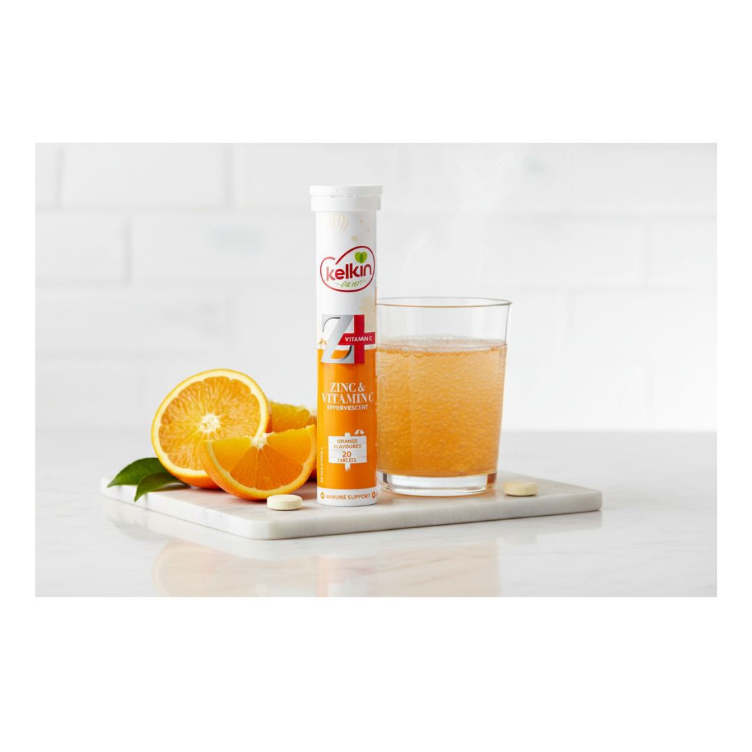 Kelkin Zinc and Vitamin C Effervescent propped up with a glass of water to the right and sliced oranges to the left