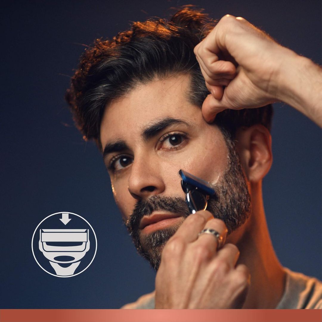 Man shaving his beard with a razor, with a dark blue background and a logo in the corner.