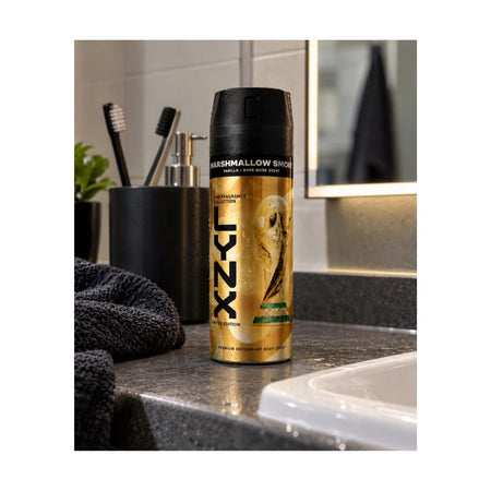 A can of LYXZ deodorant spray in Marshmallow Smoke scent, standing on a dark bathroom countertop next to a sink, toothbrush holder, and towel.