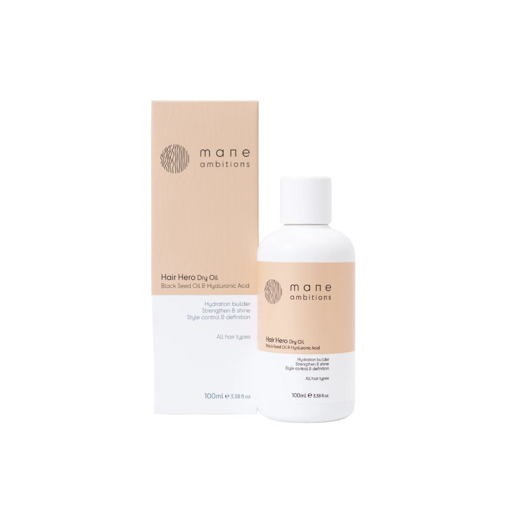 A bottle of Mane Ambitions Hair Hero Dry Oil next to its beige and white packaging box, set against a plain white background.