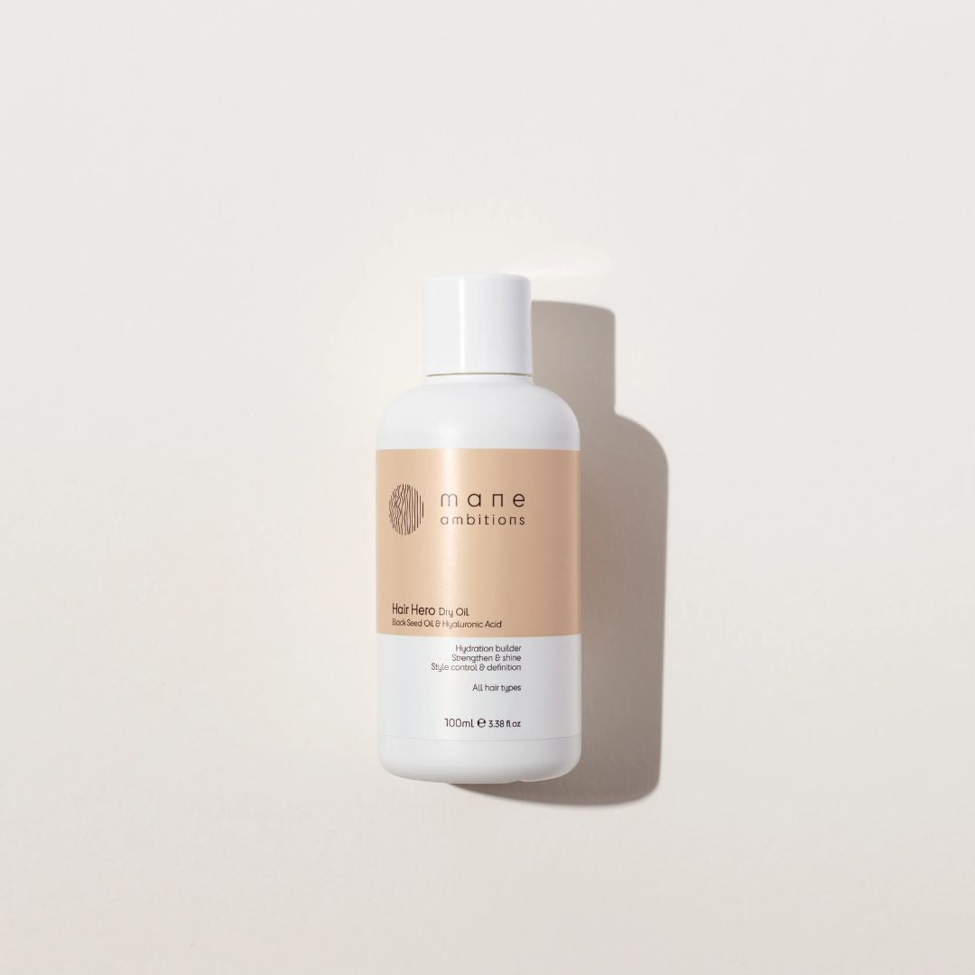 A 100ml bottle of mane combinator hair hair oil, featuring a white bottle with a beige label, set against a warm off-white background with a soft shadow.