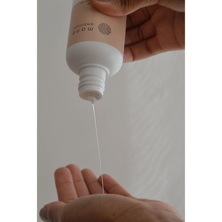 A hand holding a beige and white bottle of hair conditioner, with a thin stream of clear conditioner being poured into an open palm below.