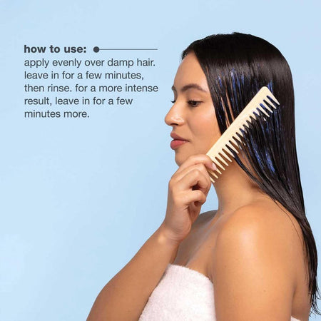 Woman applying hair product with a comb against a light blue background
