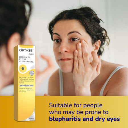 A woman touching her face stands in front of a mirror while a box of OPTASE Manuka Oil Eyelid Cleansing Gel is shown beside her. The box is yellow and white, and the image includes a yellow banner at the bottom with blue text stating it is suitable for people who may be prone to blepharitis and dry eyes.