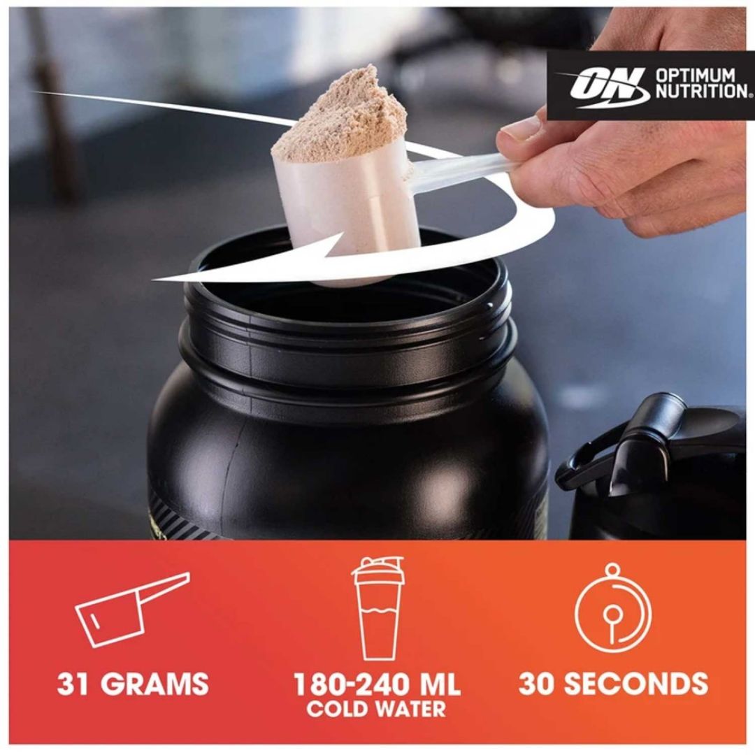 A hand using a scoop to add Optimum Nutrition powder into a large black shaker bottle, with a white arrow indicating the motion. The bottom features an orange banner with white icons and text stating '31 GRAMS', '180-240 ML COLD WATER', and '30 SECONDS'.