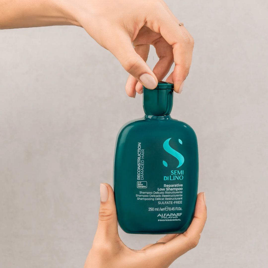 Person holding a teal shampoo bottle with a visible brand logo against a neutral background