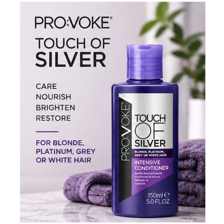 A bottle of Pro:Voke Touch of Silver Intensive Conditioner for blonde, platinum, grey, or white hair, shown next to folded purple towels and a blurred green plant on a light background.