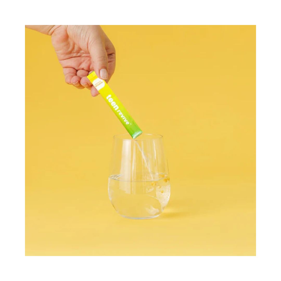 Revive Active Teen Revive Tropical being poured into a glass of water on a green background