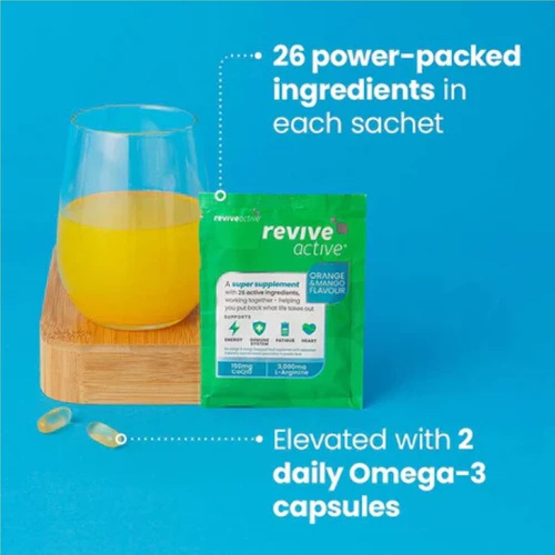 A green Revive Active orange-flavored supplement sachet stands on a blue background next to a glass of orange drink on a wooden coaster, with text callouts about 26 power-packed ingredients and 2 daily Omega-3 capsules.