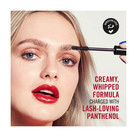 Close-up of a woman applying brow mascara with a black wand. The image includes text reading 'Creamy, Whipped Formula Charged with Lash-Loving Panthenol' and a black circular badge that says 'Sensitive Eyes'.