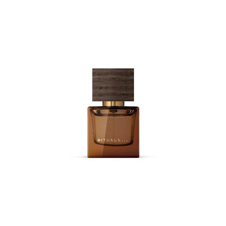 A rectangular amber-brown glass perfume bottle with a dark wood-grain cap and gold lettering that reads 'RITUALS...'.