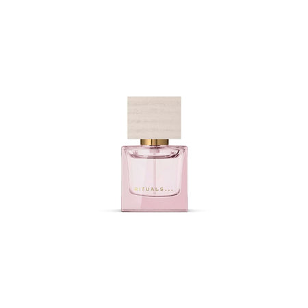 A pink glass perfume bottle with a light wood-textured cap and gold lettering that reads 'RITUALS.