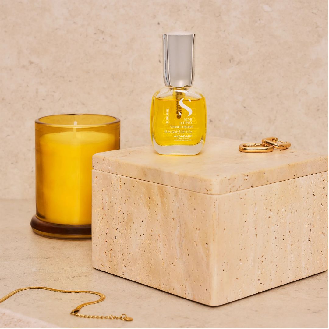 A bottle of Scented Scents 'Scent of the Sea' amber perfume oil with a silver cap, displayed on a beige stone box next to a yellow candle and gold jewelry.