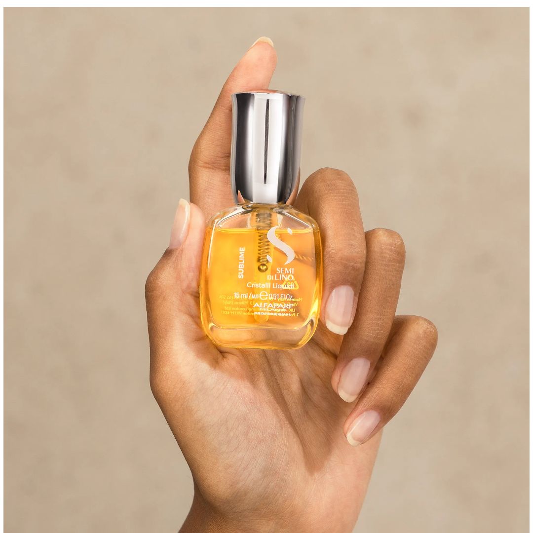 A hand holding a small bottle of Oribe Palm Oil Hand and Face Cream against a neutral beige background.