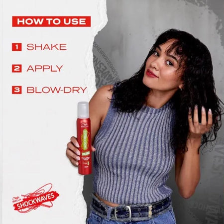 A woman holding a red Shockwaves hair product can, with on-image text showing how to use it: shake, apply, and blow-dry. The background is a split design with a white torn-paper section on the left and a gray textured wall on the right.